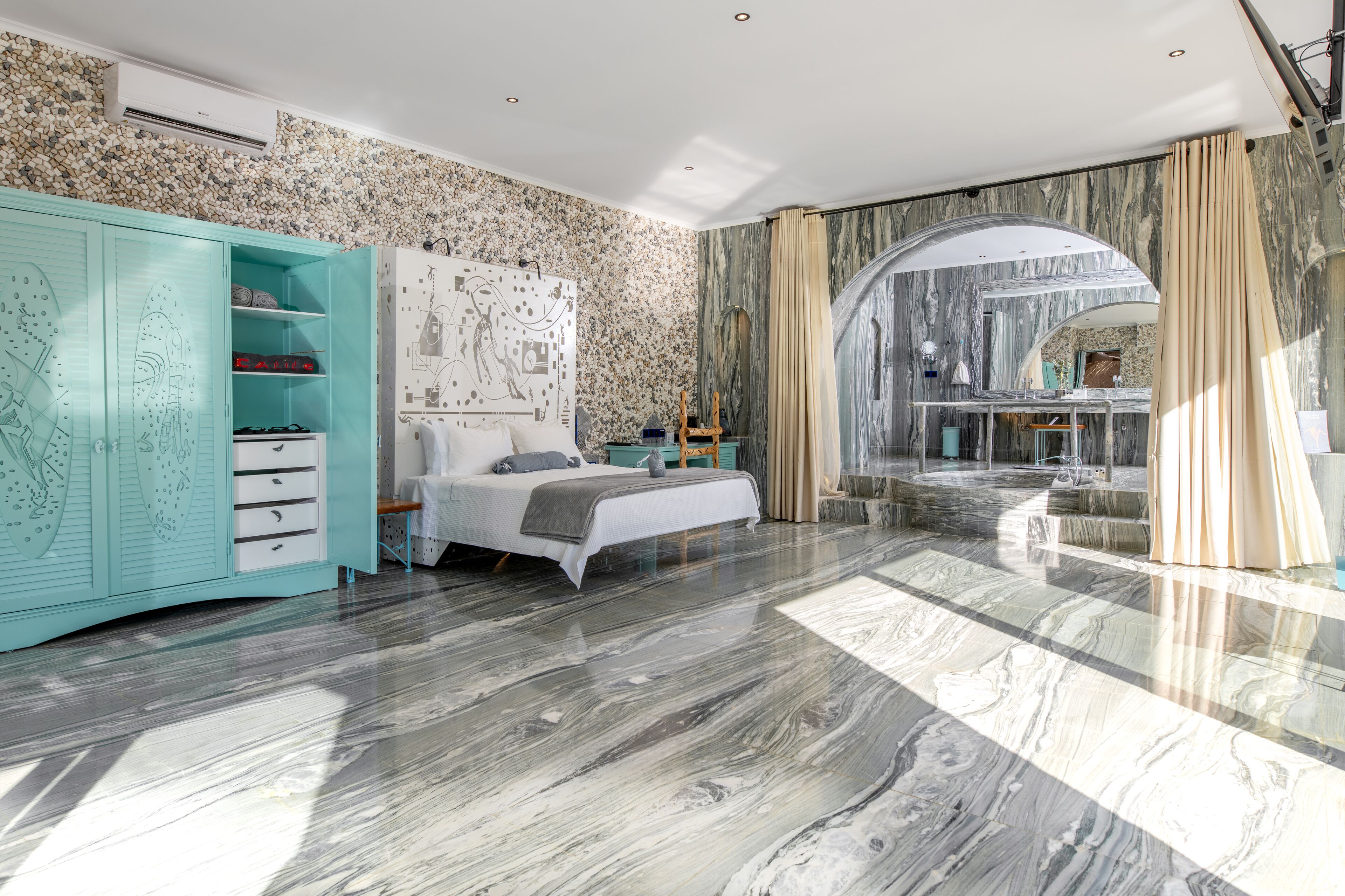 A modern bedroom with a large bed, a teal wardrobe, and a marble floor.