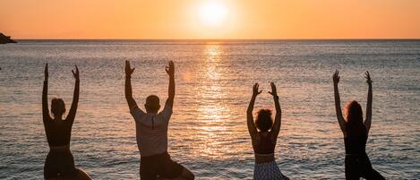 Four people practicing yoga on mats at the beach during sunset.