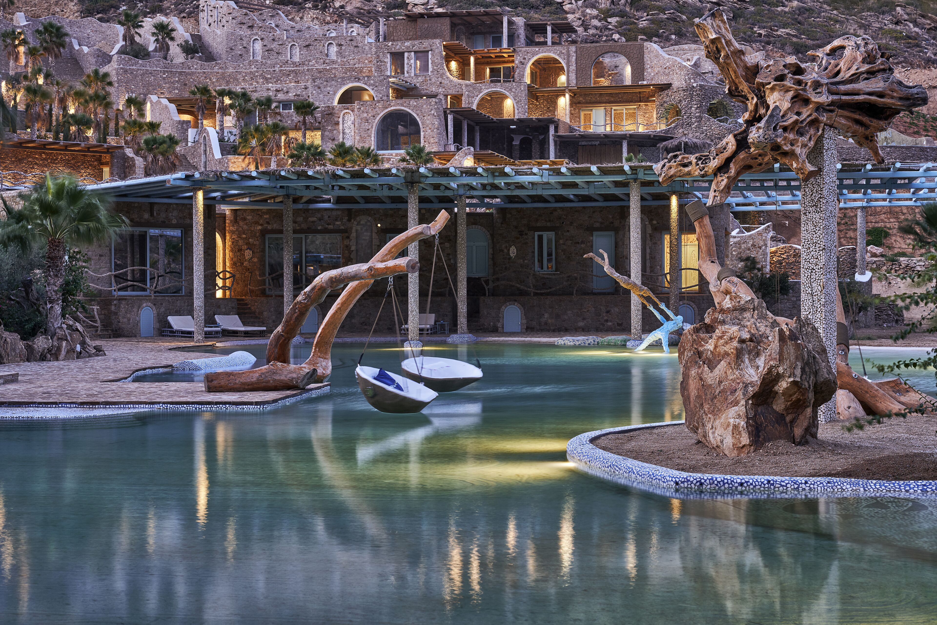 A pool area with unique wooden sculptures, a clear view of a building with arched windows, and a well-maintained landscape.