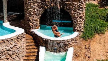 Ein Steinelement mit mehreren Pools und einer zentralen Fontäne, umgeben von einer rustikalen Steinarchitektur.