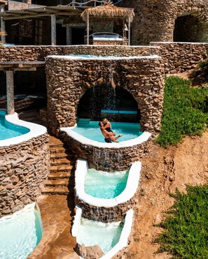 A stone water feature with multiple pools and a central fountain, surrounded by a rustic stone structure.