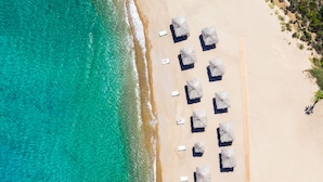 An aerial view of a beach with rows of sun loungers and umbrellas, a wooden walkway, and clear turquoise water. - Calilo (Ios)