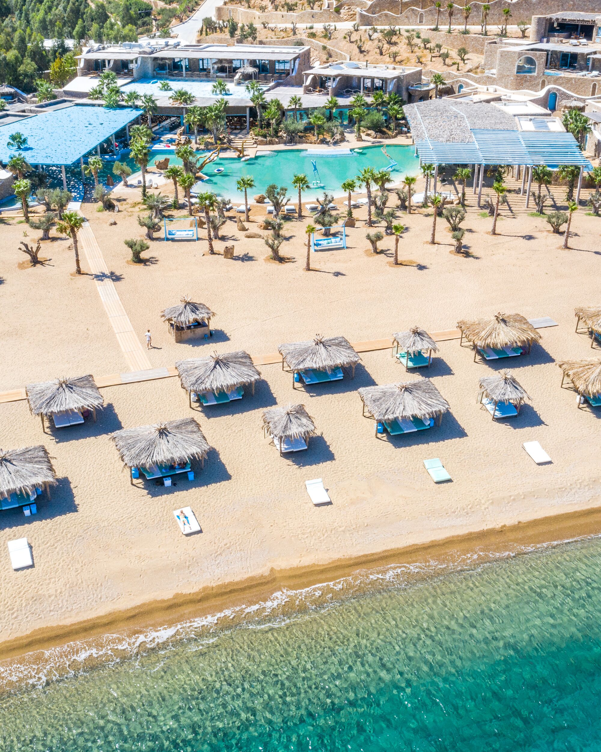 A beach resort with multiple pools, sun loungers, and thatched umbrellas.
