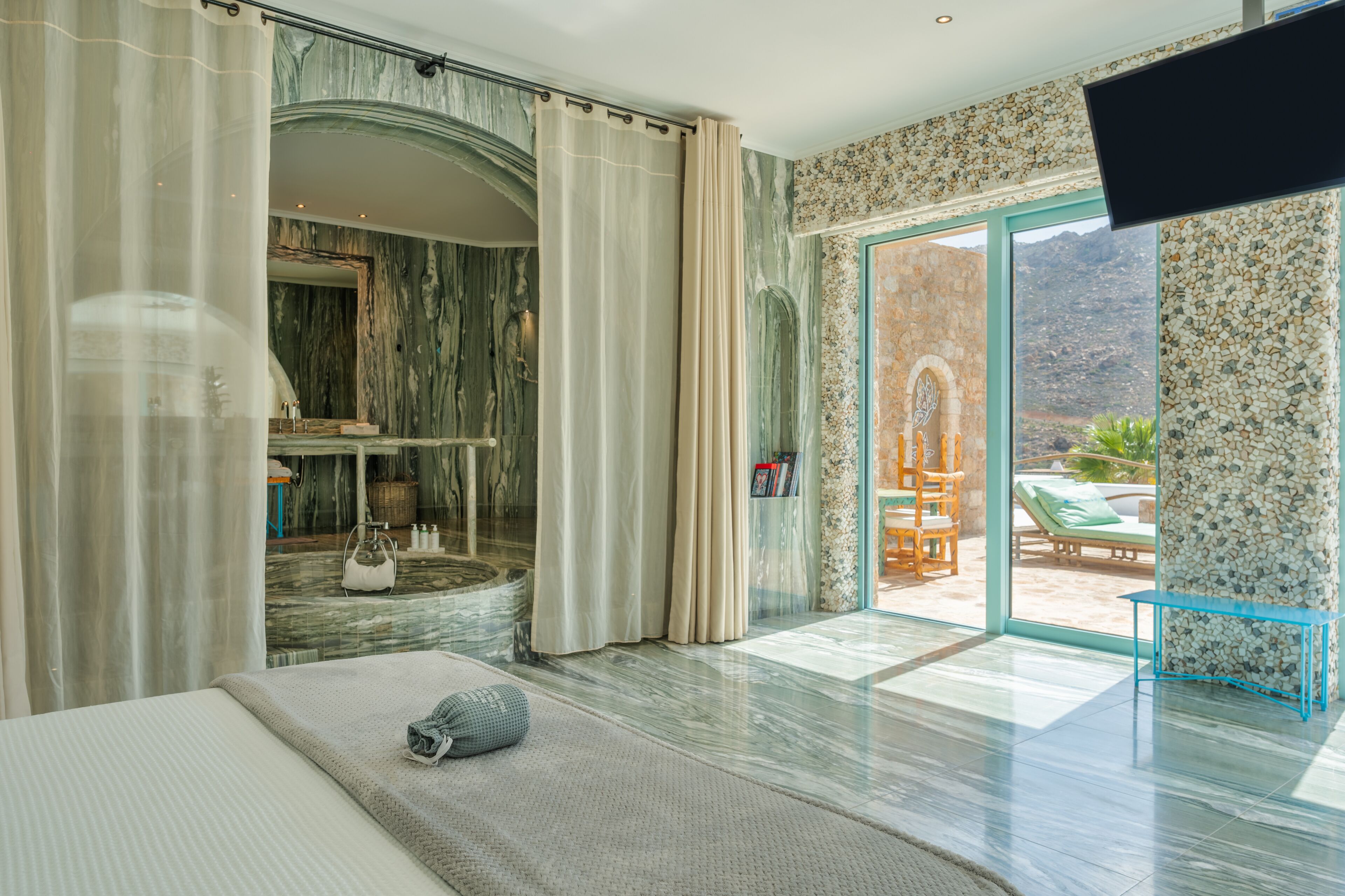 Una habitación amplia con una cama grande, una pared de mármol y vistas a la zona de la piscina.