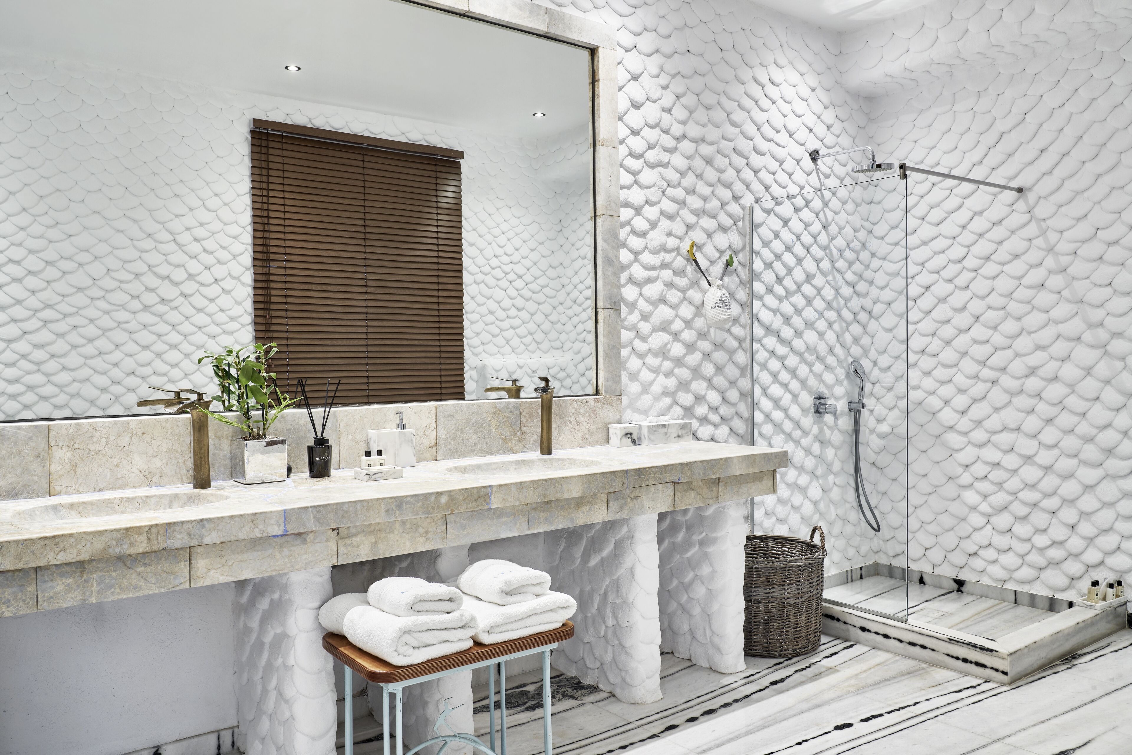 Un baño moderno con pared blanca texturizada, un espejo grande, encimera de mármol y zona de ducha.