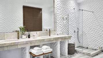 Un baño moderno con pared blanca texturizada, un espejo grande, encimera de mármol y zona de ducha.