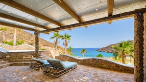 A stone-floored patio with two sun loungers and a stone wall overlooking a coastal view. - Calilo (Ios)