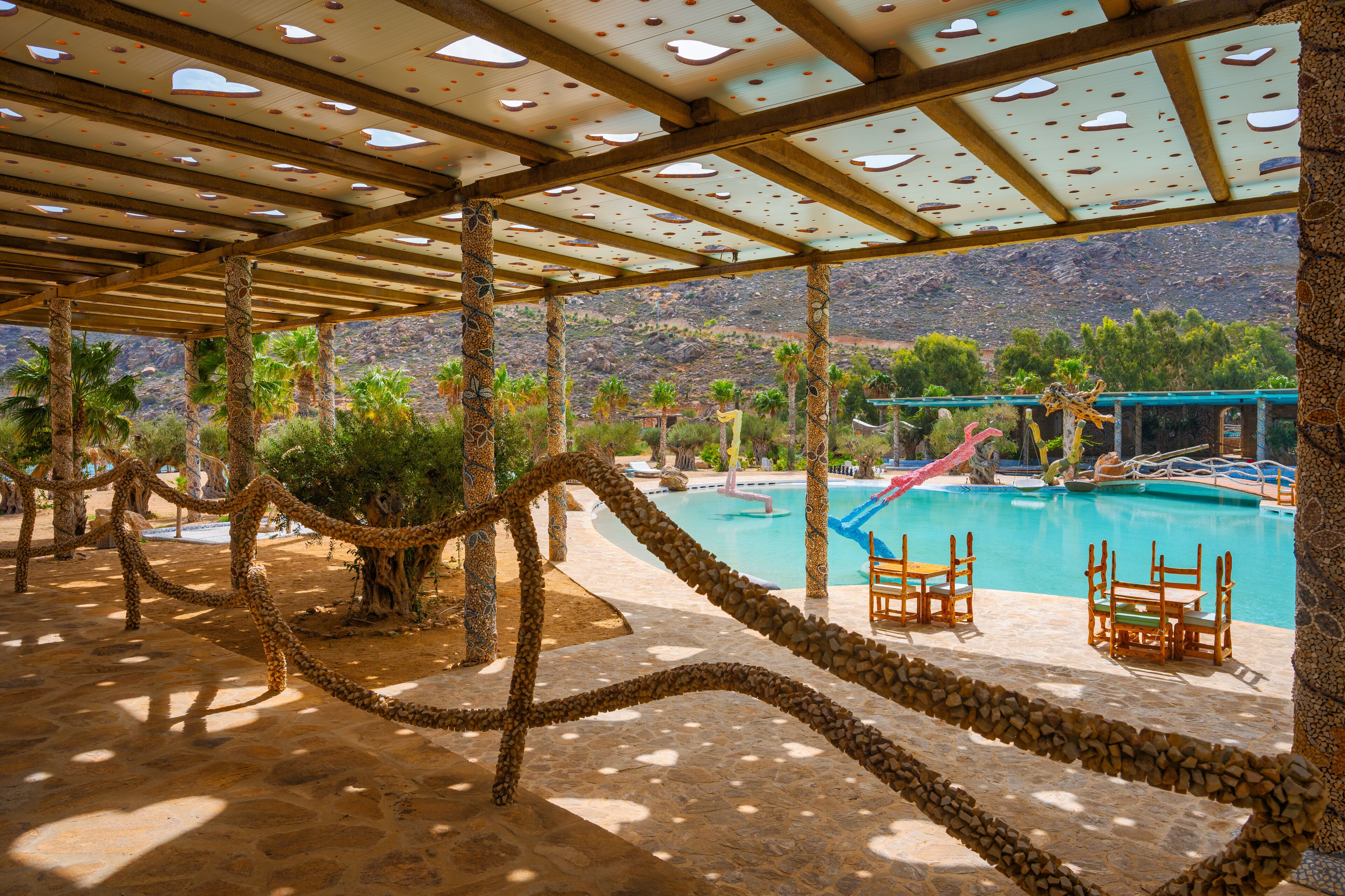A pool area with stone pillars, a rope barrier, and wooden chairs.