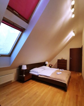 A bedroom with a sloped ceiling, a bed, bedside tables, a dresser, and a window.
