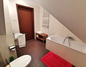 A modern bathroom with a bathtub, toilet, and a wooden shelf with towels.