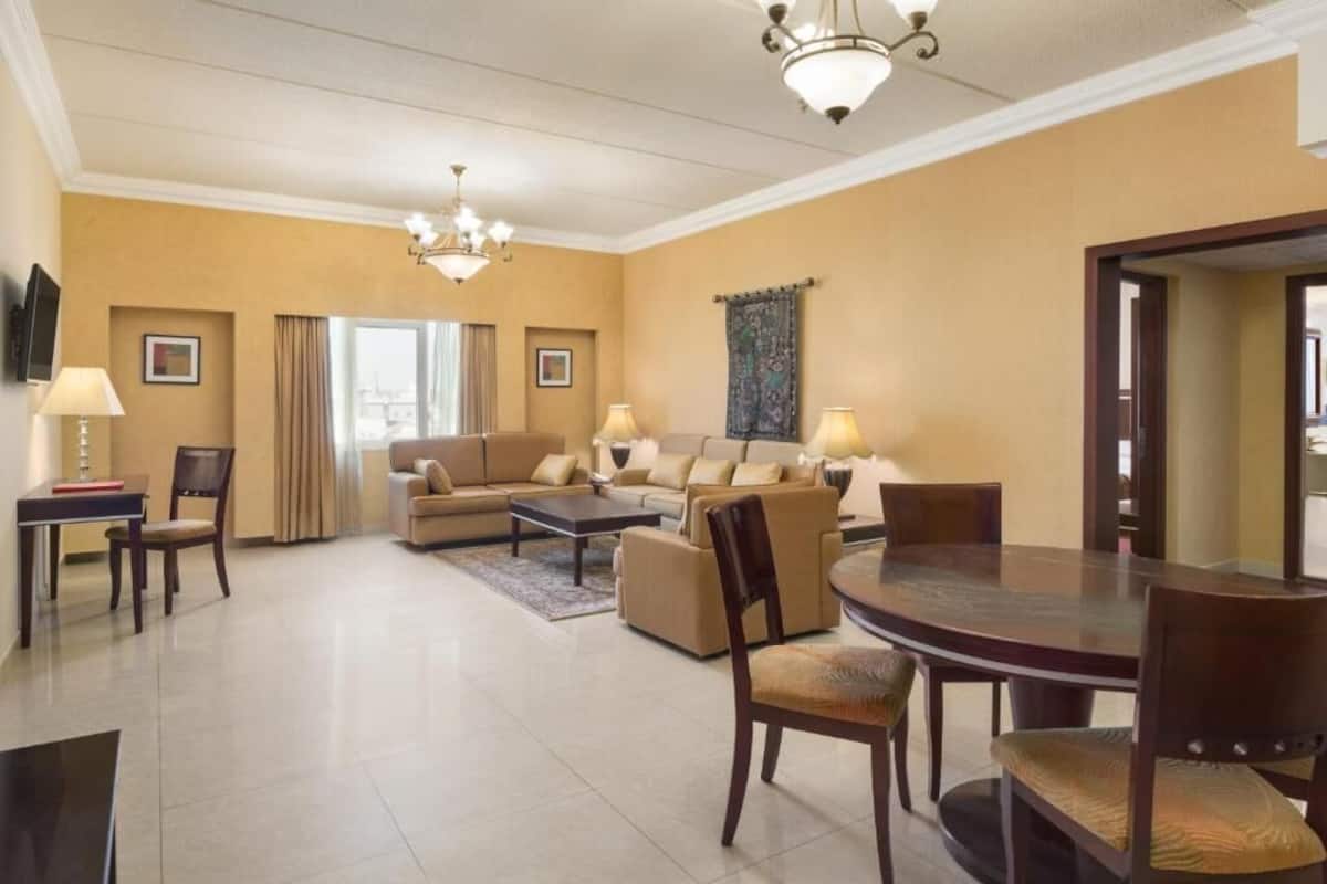A spacious living room with a sofa set, a dining table, and a TV mounted on the wall.
