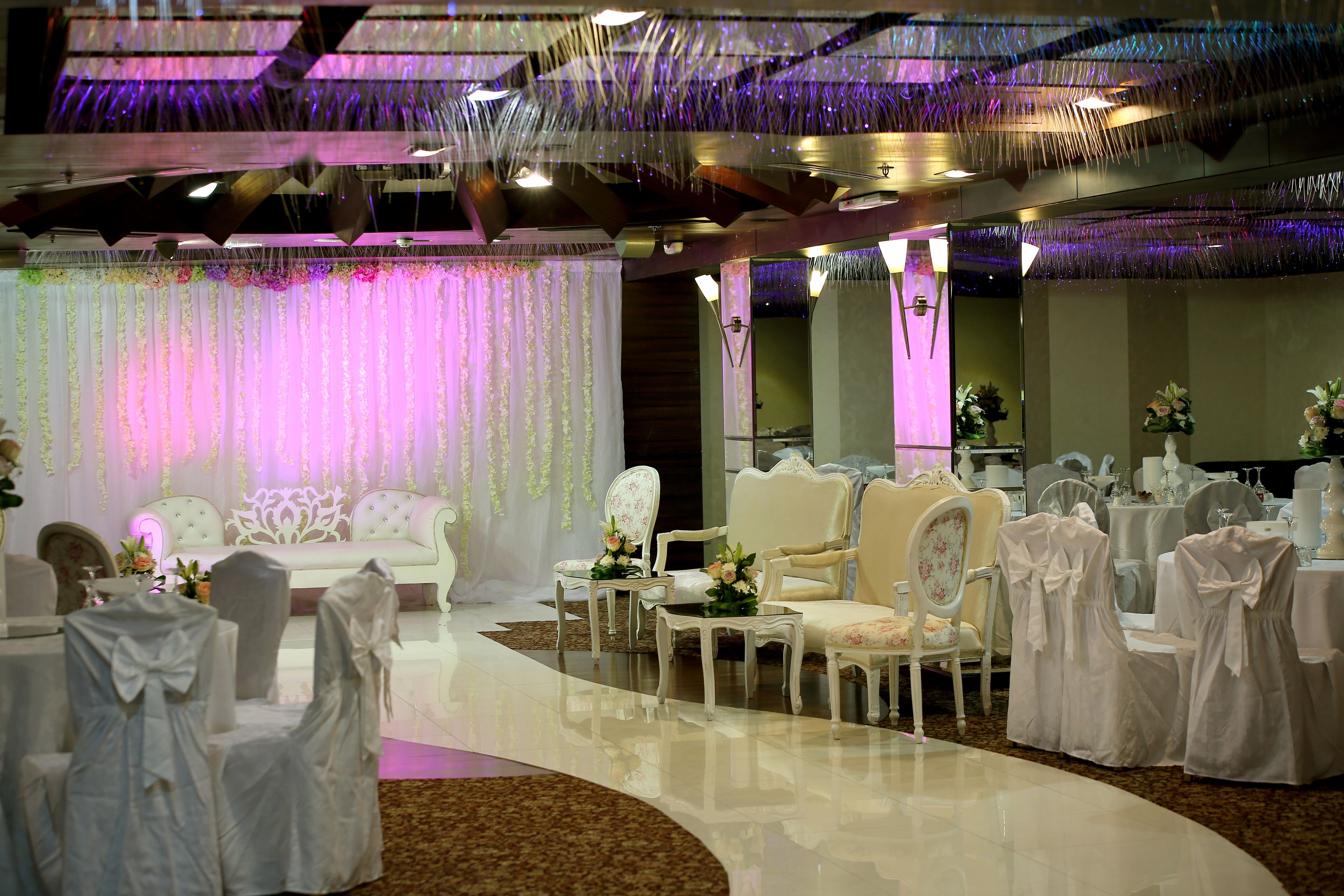 Un espacio para eventos formales con sillas y mesas blancas, elegantes arreglos florales y un decorado ornamental.