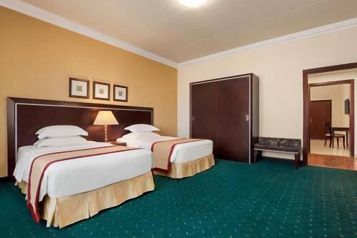 A hotel room with two beds, a desk, a chair, and a wardrobe.