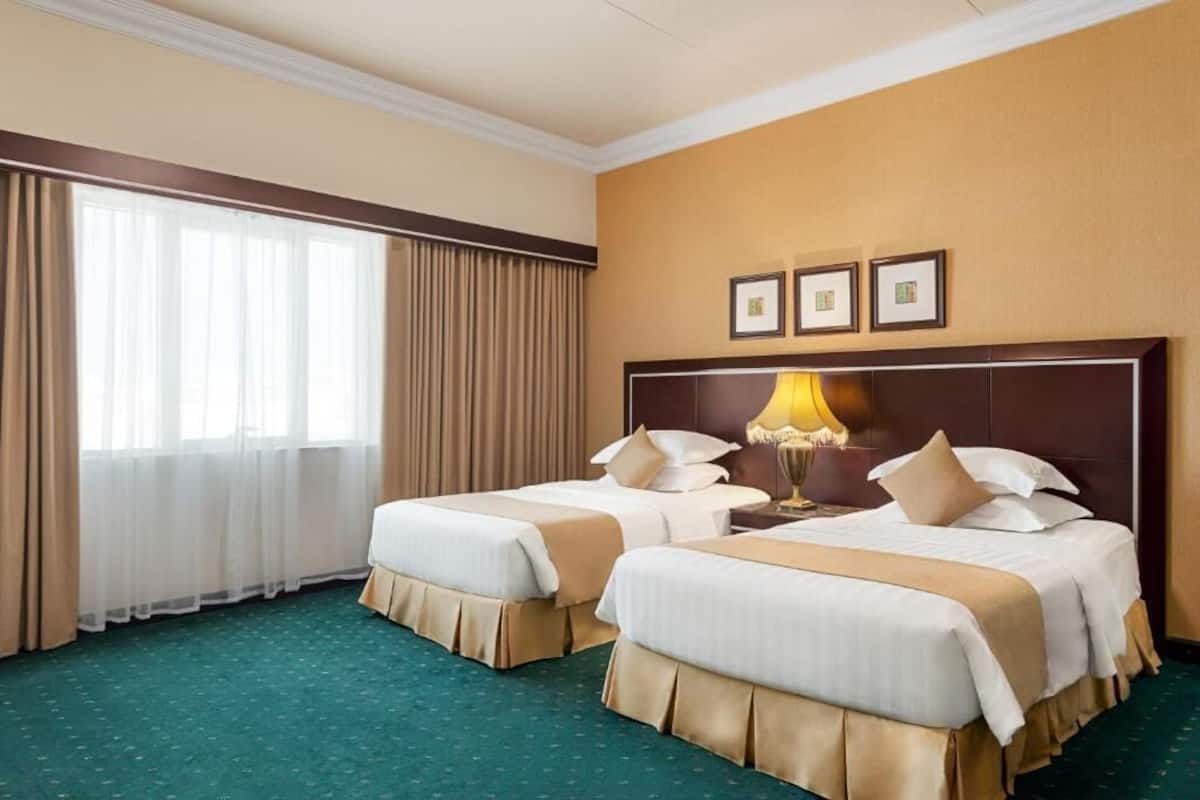 A hotel room with two beds, a large window with curtains, and a wall with three framed pictures.