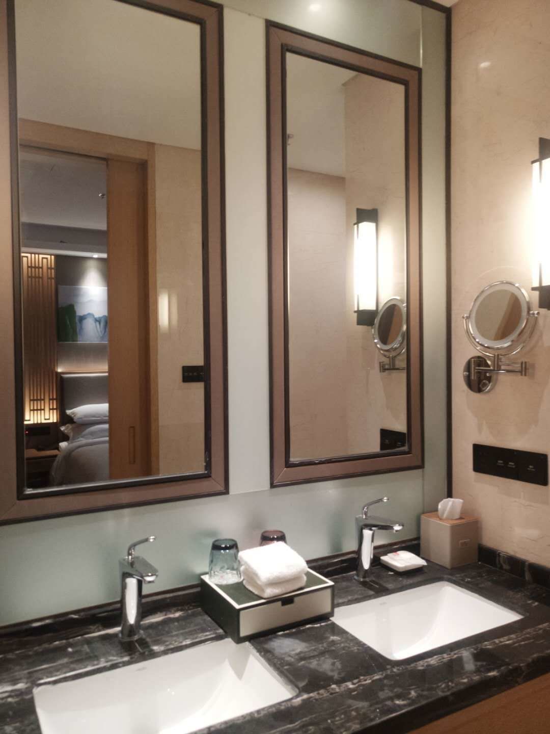 A hotel bathroom with two sinks, a large mirror, and a small mirror above the sink.