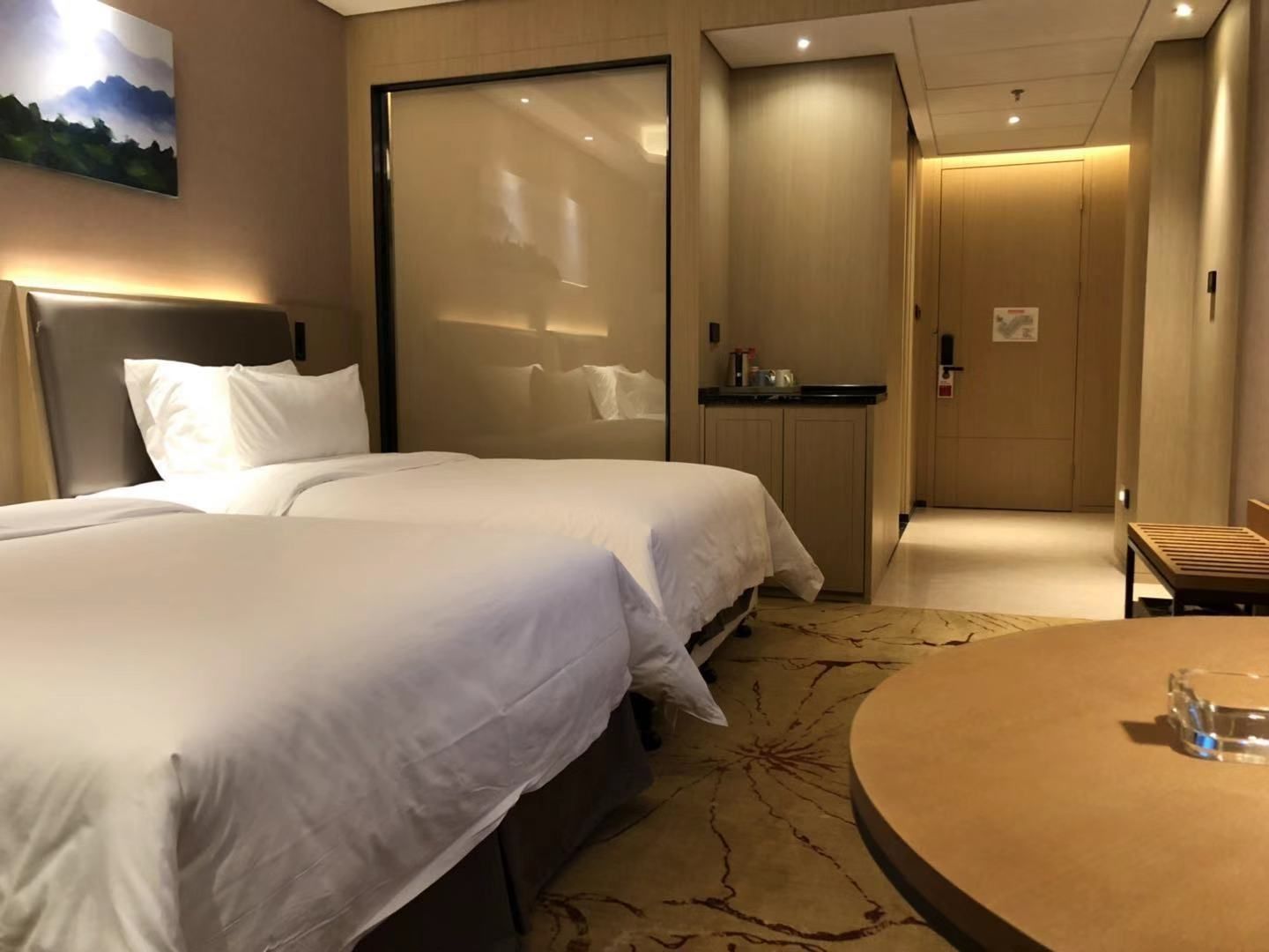 A hotel room with two beds, a small kitchenette, and a round table.