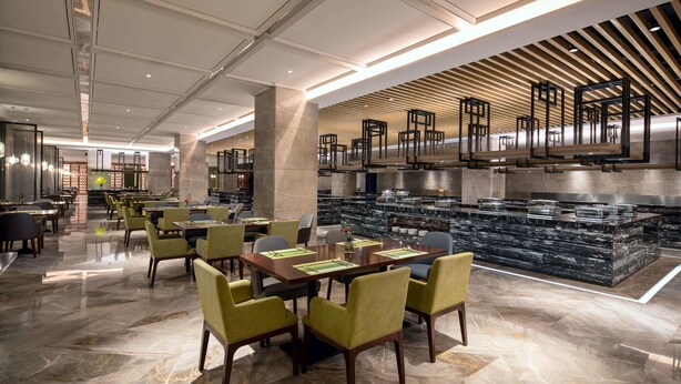 A modern hotel lobby with marble flooring, green upholstered chairs, and a central bar area with a granite countertop. - Ramada Wyndham Zhengzhou Xinzheng (Zhengzhou)