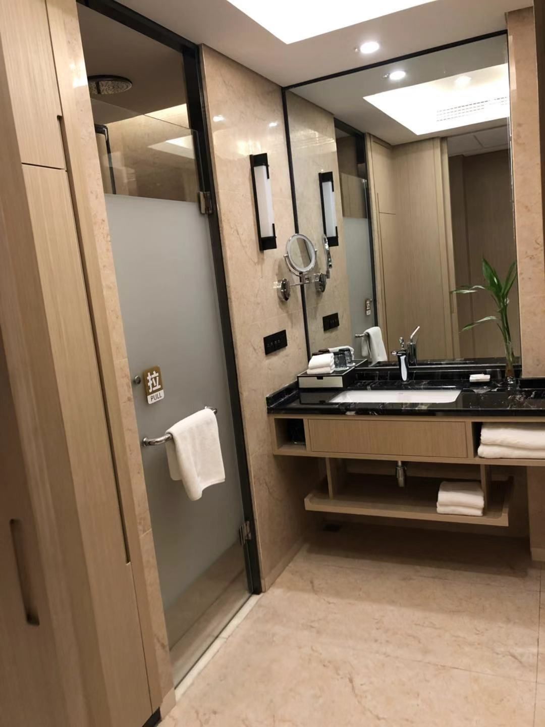 A modern bathroom with a glass shower door, a large mirror, and a black countertop with a sink.