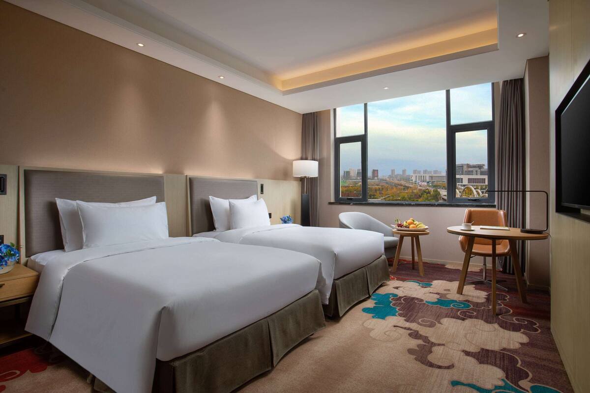 Ein Hotelzimmer mit zwei Betten, einem kleinen Tisch mit Früchten, einem Sessel und einem Fernseher.
