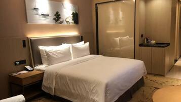 Une chambre d’hôtel avec un grand lit, une table de chevet avec un téléphone, un petit bureau, une chaise, une table ronde et un tableau au mur.