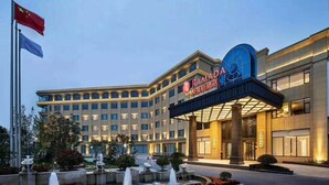A modern hotel with a prominent entrance, a fountain, and a flag. - Ramada Wyndham Zhengzhou Xinzheng (Zhengzhou)