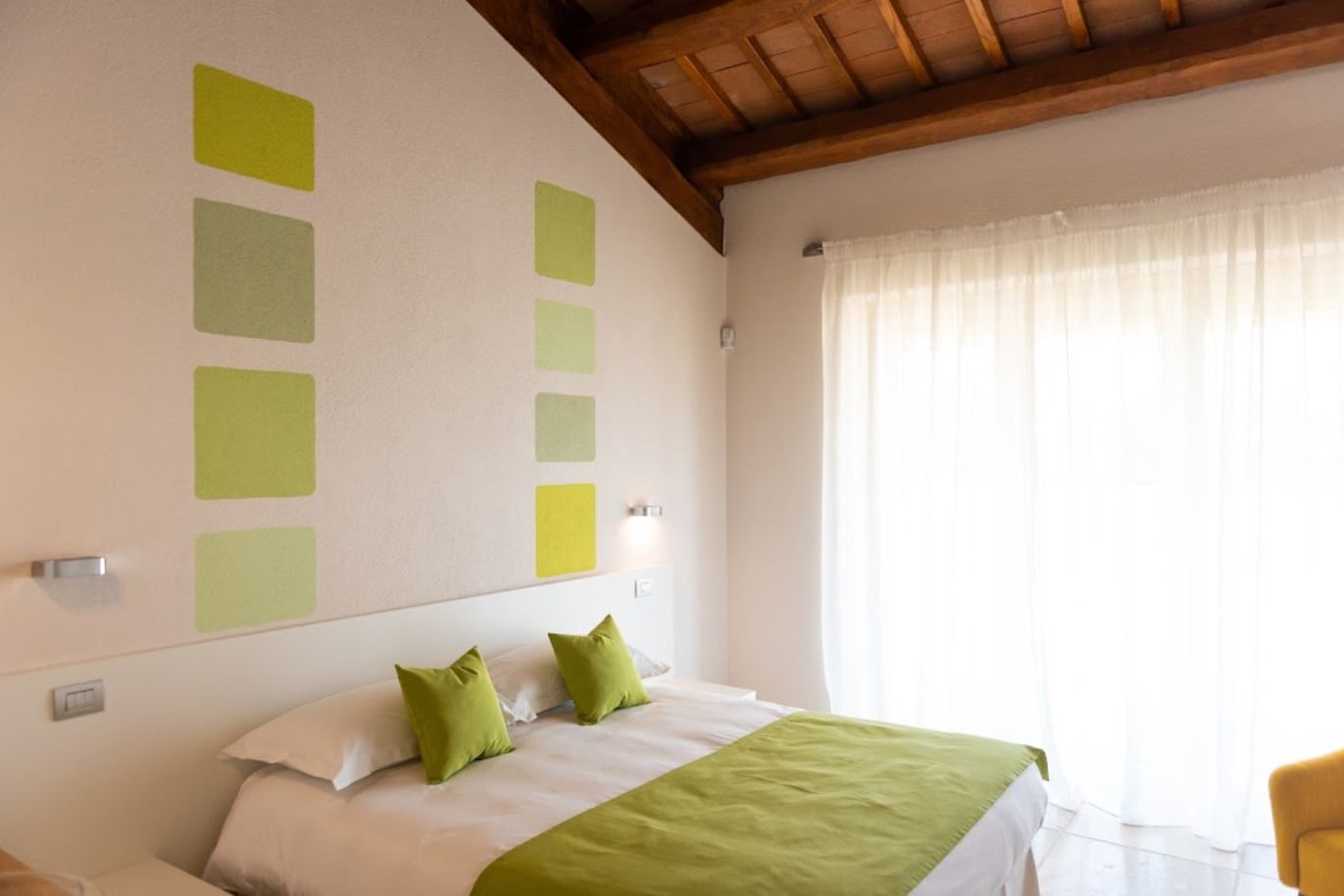 A bedroom with a bed, green pillows, a green throw blanket, and a window with curtains.