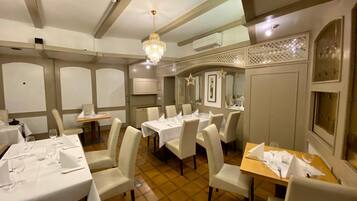 A restaurant with multiple tables set for dining, a chandelier, and a decorative wall.