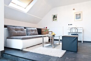 Un salon moderne avec un canapé, une table basse en verre, une petite table d’appoint, un radiateur et un tableau encadré accroché au mur.