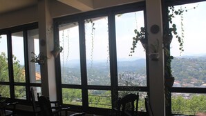 A room with large windows overlooking a scenic landscape, furnished with chairs and potted plants. - Lawan One Kandy (Kandy)