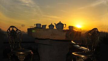 A table with teapots and cups on a stone ledge against a sunset.