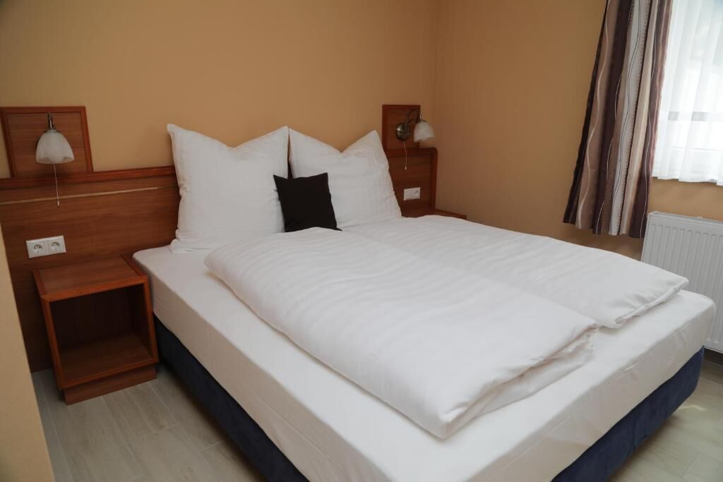 Quarto de hotel com cama, cabeceira de madeira, mesas de cabeceira, abajures e uma janela com cortinas.