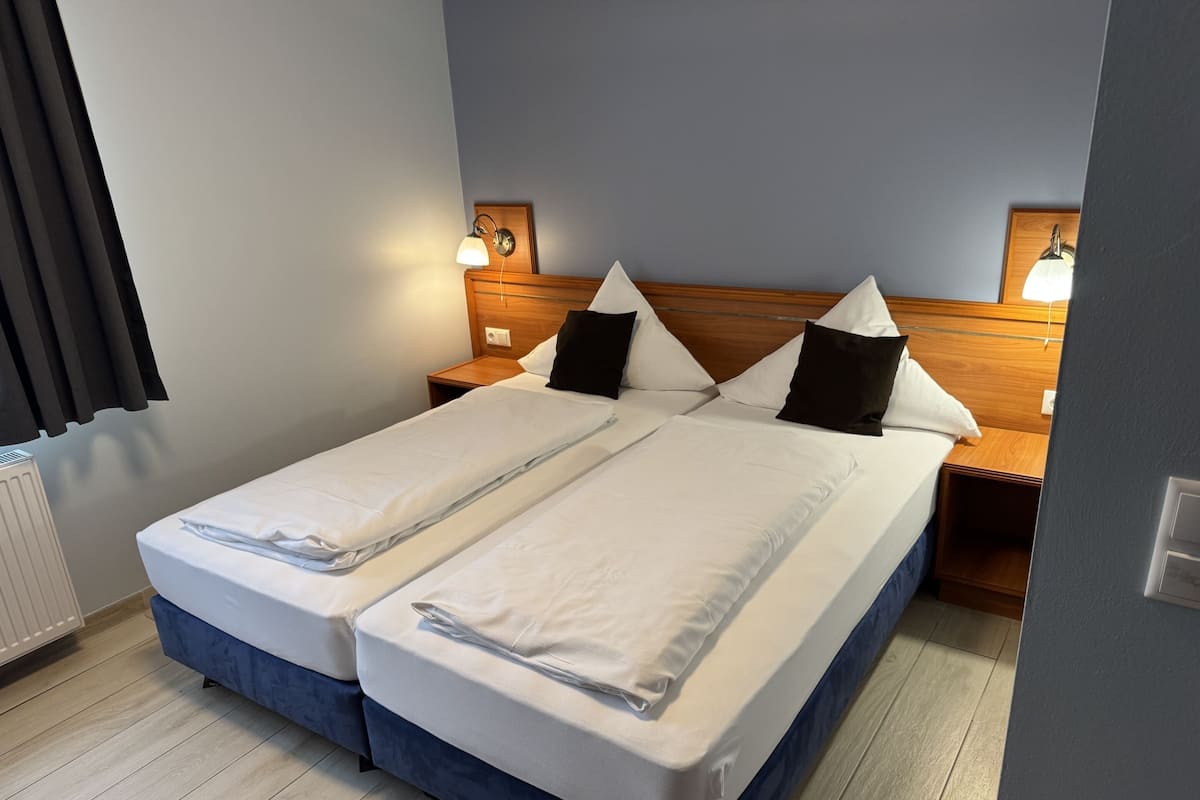 A double bed with white linens, a wooden headboard, bedside lamps, and a radiator.