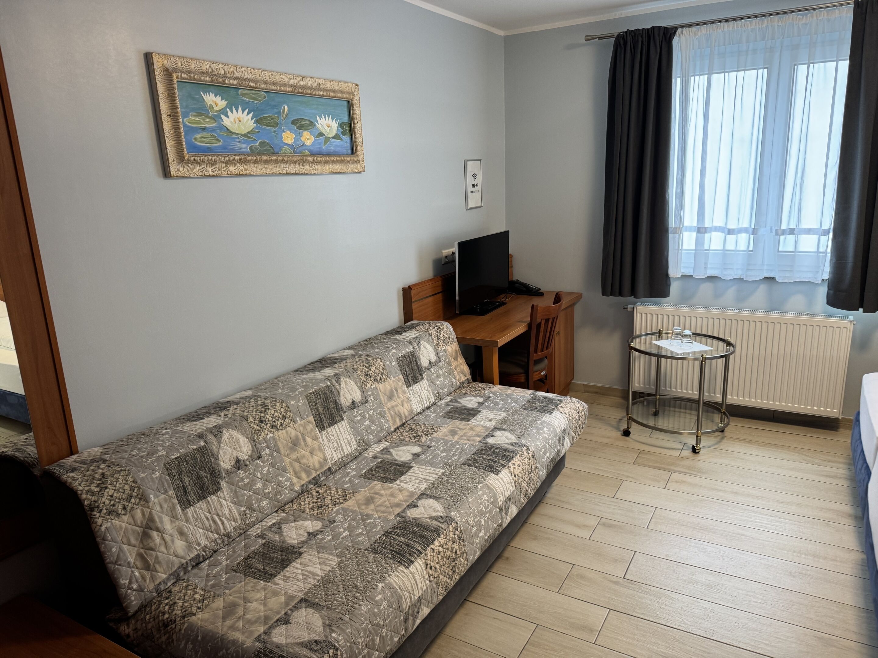 A room with a sofa, a small desk with a computer, a radiator, and a window with curtains.