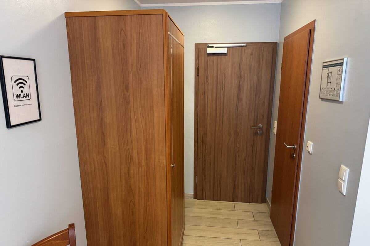 A hallway with wooden doors, a framed WLAN sign, and a small electrical outlet on the wall.