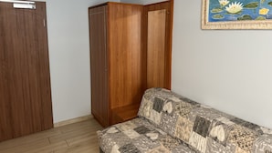 A room with a wooden wardrobe, a sofa with a patterned cover, and a framed painting of water lilies. - Hotel Mykonos (Eschweiler)