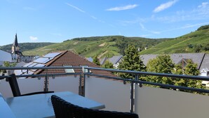 Un balcon avec une table et des chaises donnant sur un vignoble et une église.