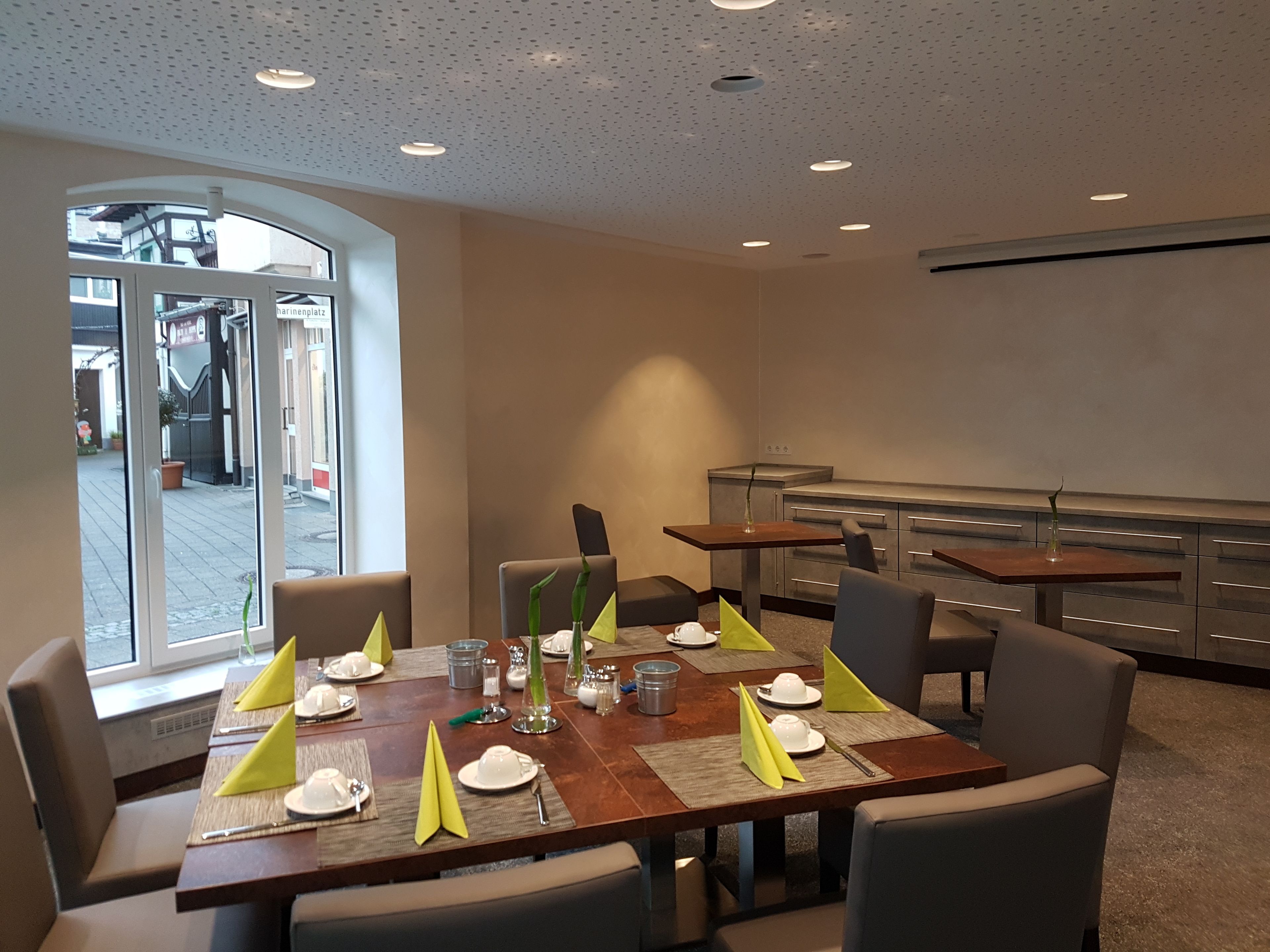 Ein Essbereich mit einem langen Tisch, gedeckt für sechs Personen, inklusive Stühle, Geschirr und einem Blumenstrauß.