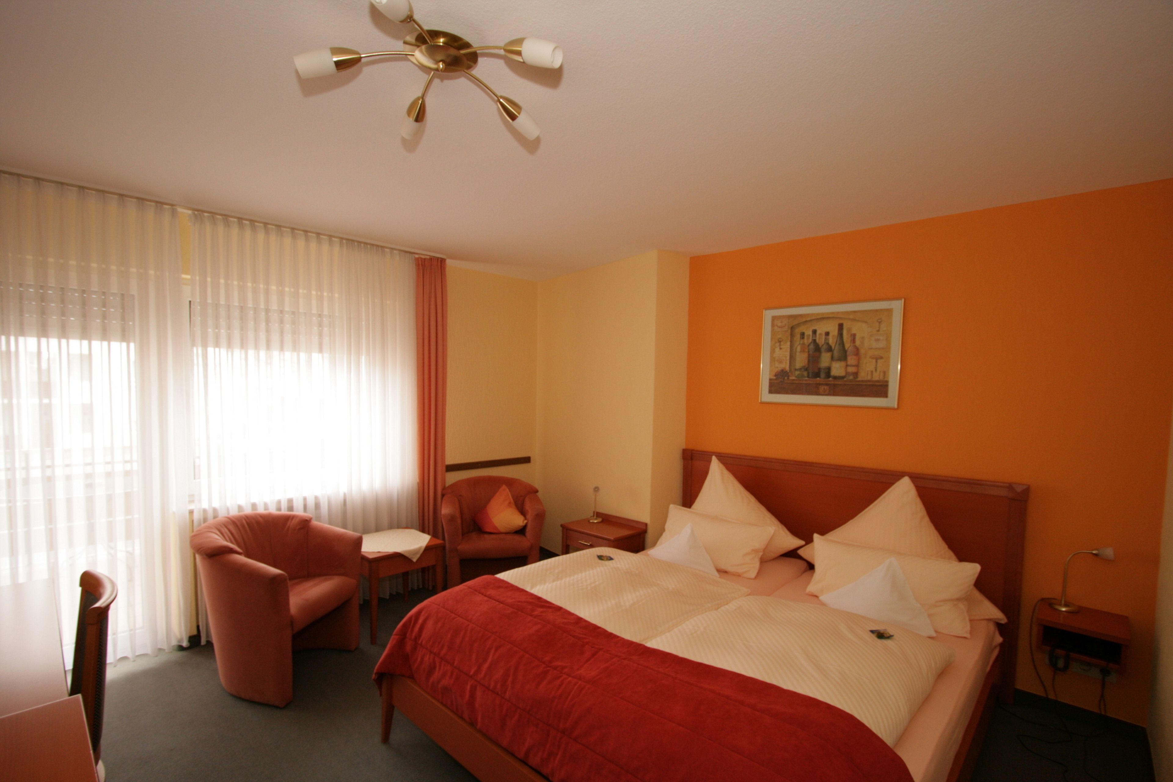 A hotel room with a large bed, a chair, a desk, and a ceiling fan.