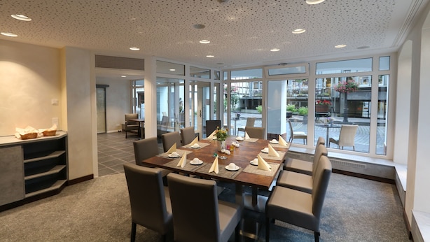 Un espace repas moderne avec une grande table dressée pour six personnes, entourée de chaises.