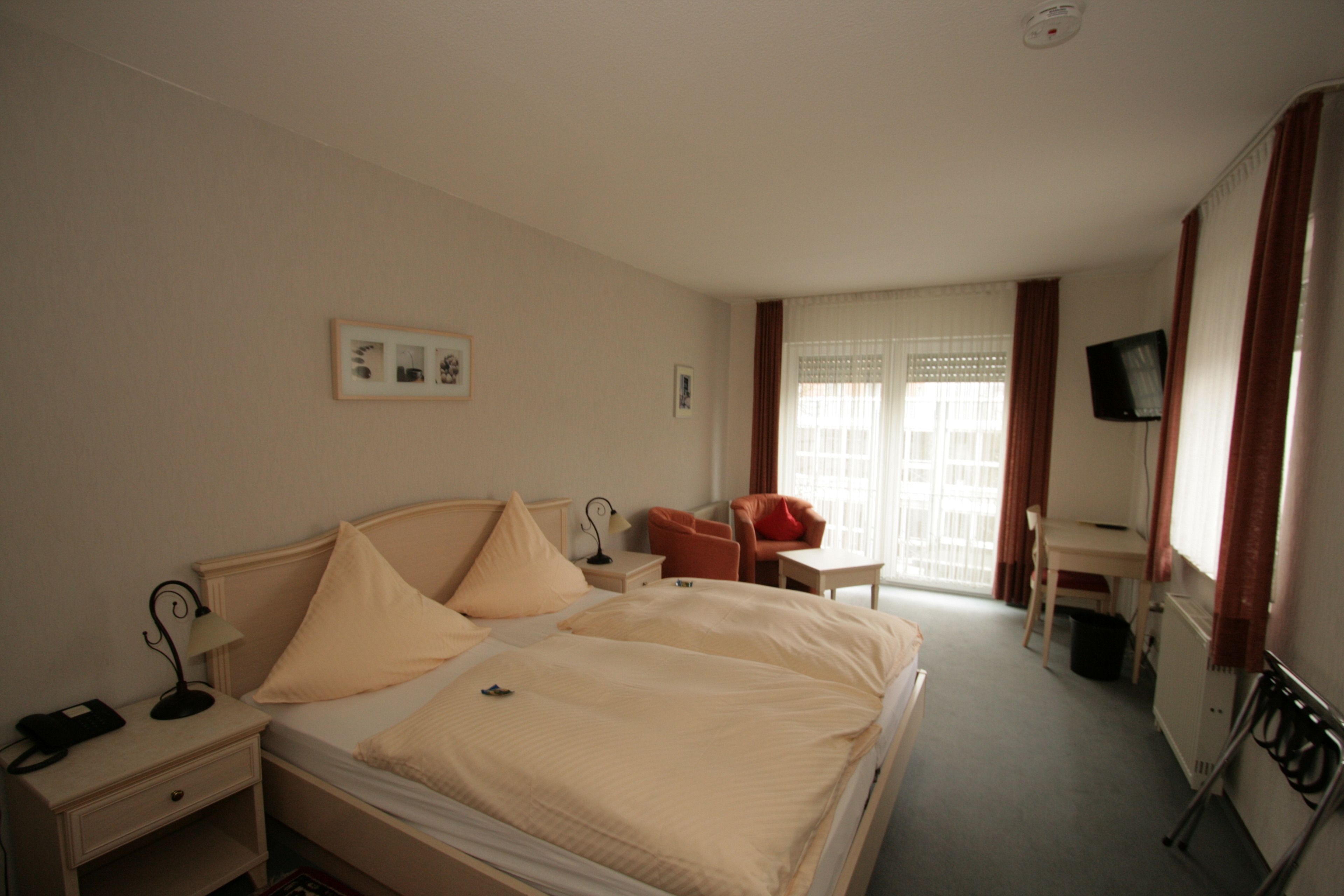 A hotel room with a bed, a desk, a chair, a TV, and a window with curtains.