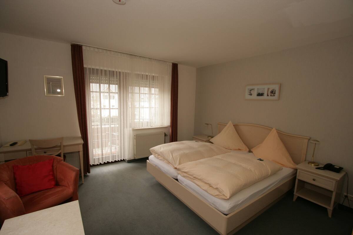 Ein Hotelzimmer mit Bett, Schreibtisch, Stuhl und einem fenster mit Vorhängen.