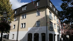Un hôtel appelé « Anchen », de style architectural classique, doté de nombreuses fenêtres et d’un balcon.