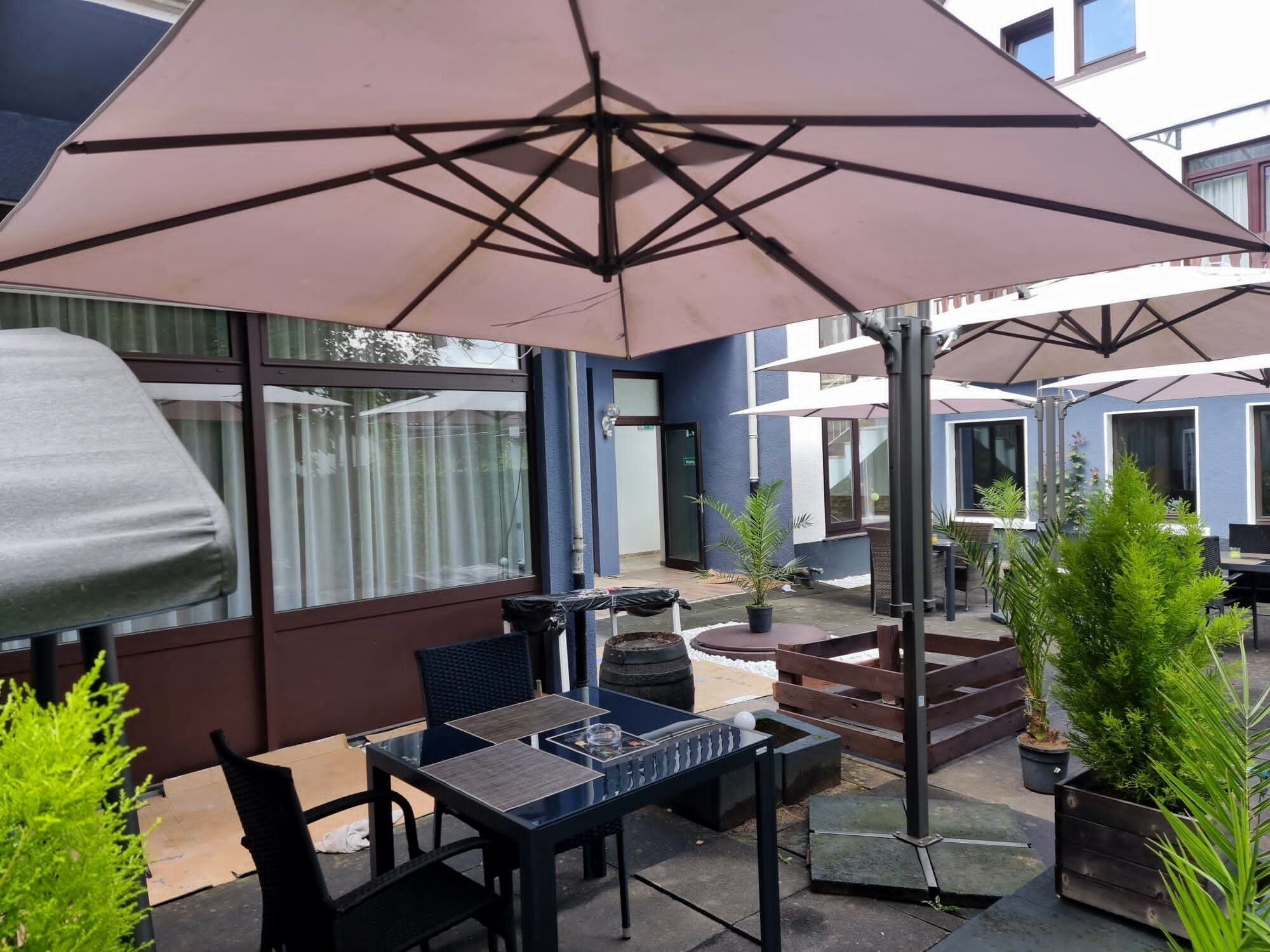Un'area patio all'aperto con tavolo e sedie, un ombrellone grande e piante in vaso.