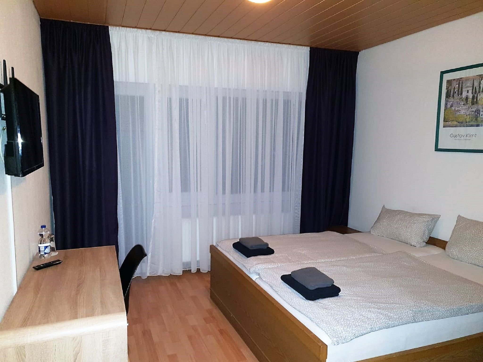 Una habitación de hotel con cama, escritorio, silla y televisión en la pared.