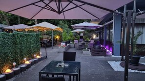 Un patio al aire libre con mesas, sillas, sombrillas e iluminación decorativa.
