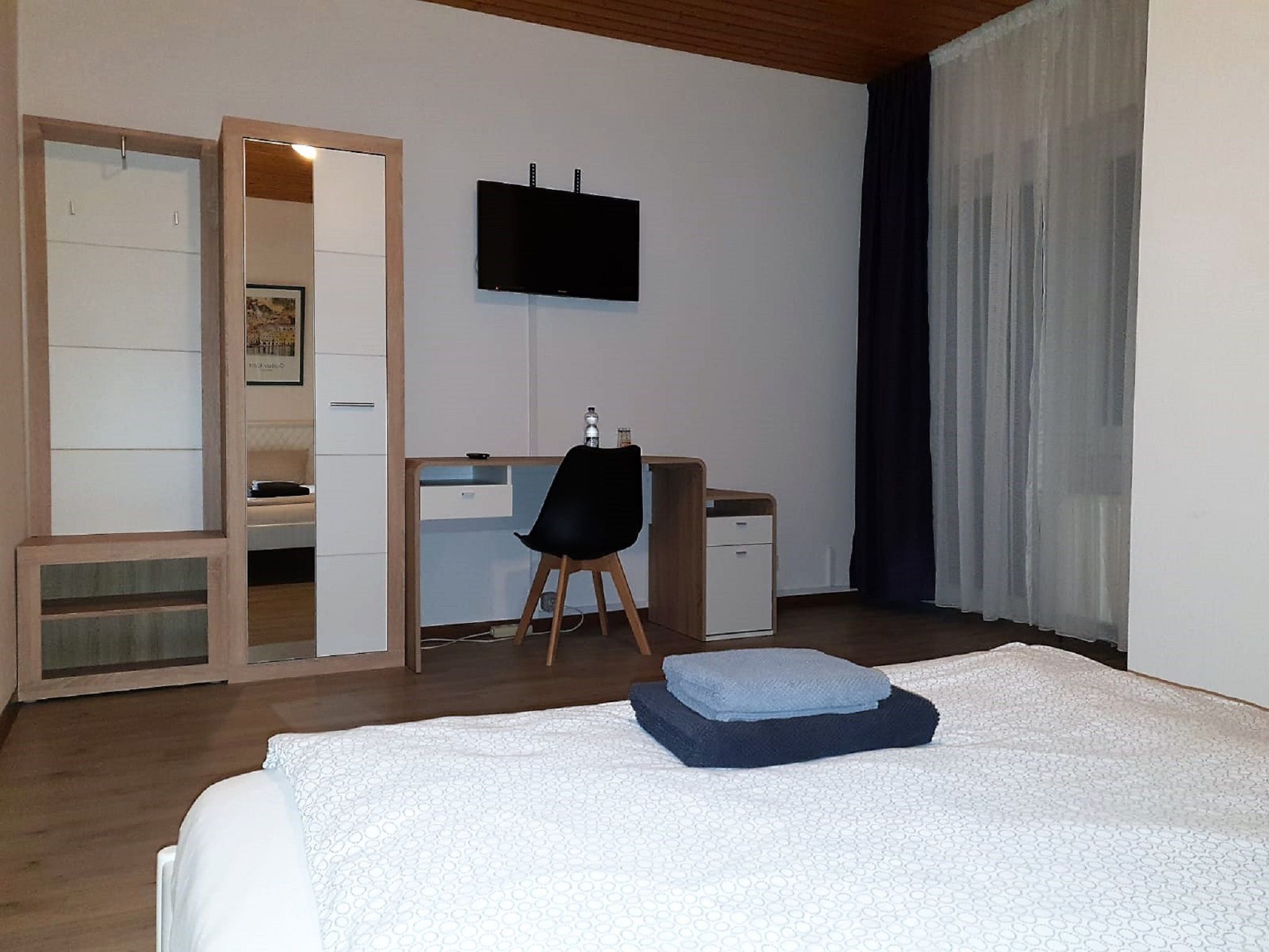 Ein Hotelzimmer mit Bett, Schreibtisch, Stuhl, Fernseher und einem Fenster mit Vorhängen.