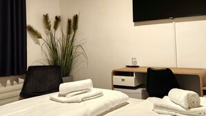 Ein Hotelzimmer mit zwei Betten, einem an der Wand befestigten Flachbildfernseher, einem hölzernen Schreibtisch und einem Blumentopf.