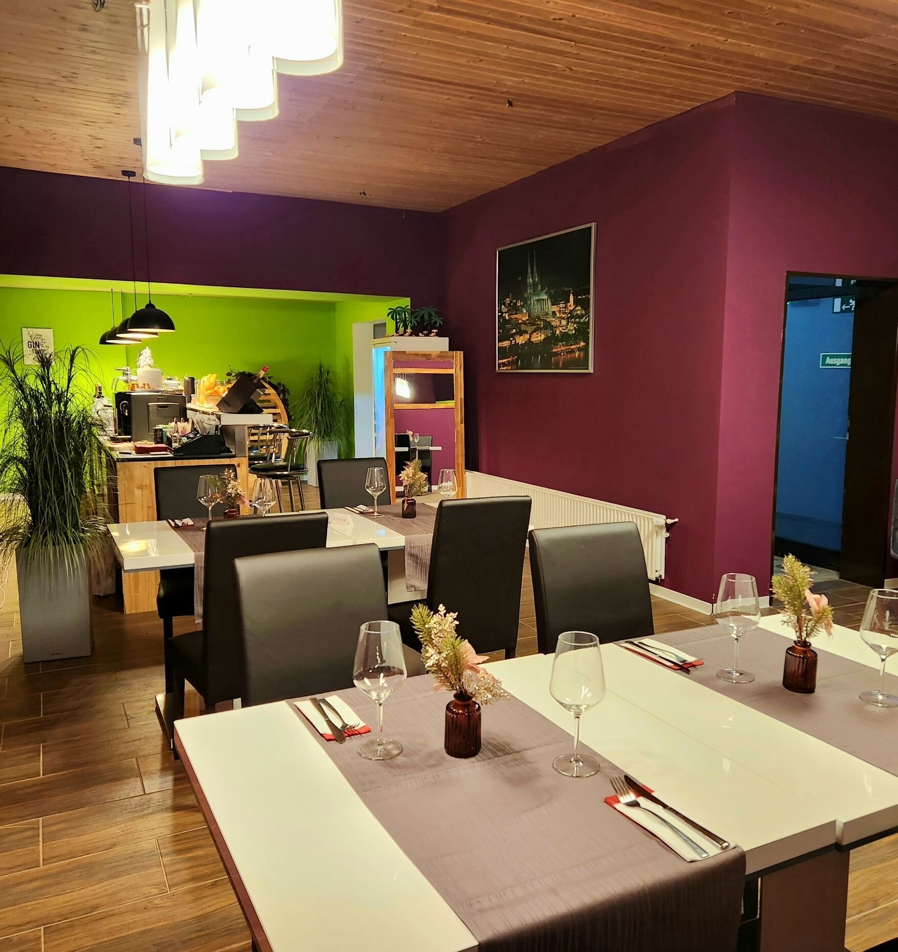 Un comedor con una mesa lista para dos personas, sillas y vista a un paisaje urbano a través de una ventana.