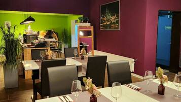 Un comedor con una mesa lista para dos personas, sillas y vista a un paisaje urbano a través de una ventana.
