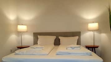 A double bed with two pillows, a bedside table with a lamp, and a wall-mounted plant.